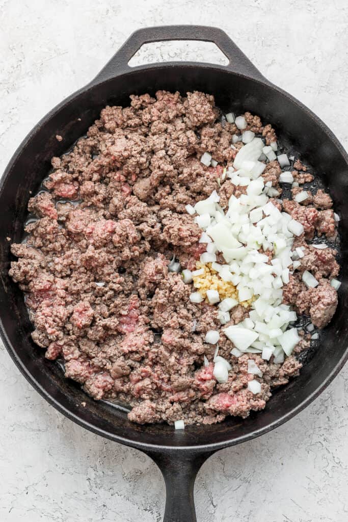 Ground beef in a skillet with diced onion and minced garlic.