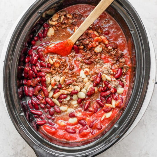 Slow cooker chili with beans, wooden spoon.