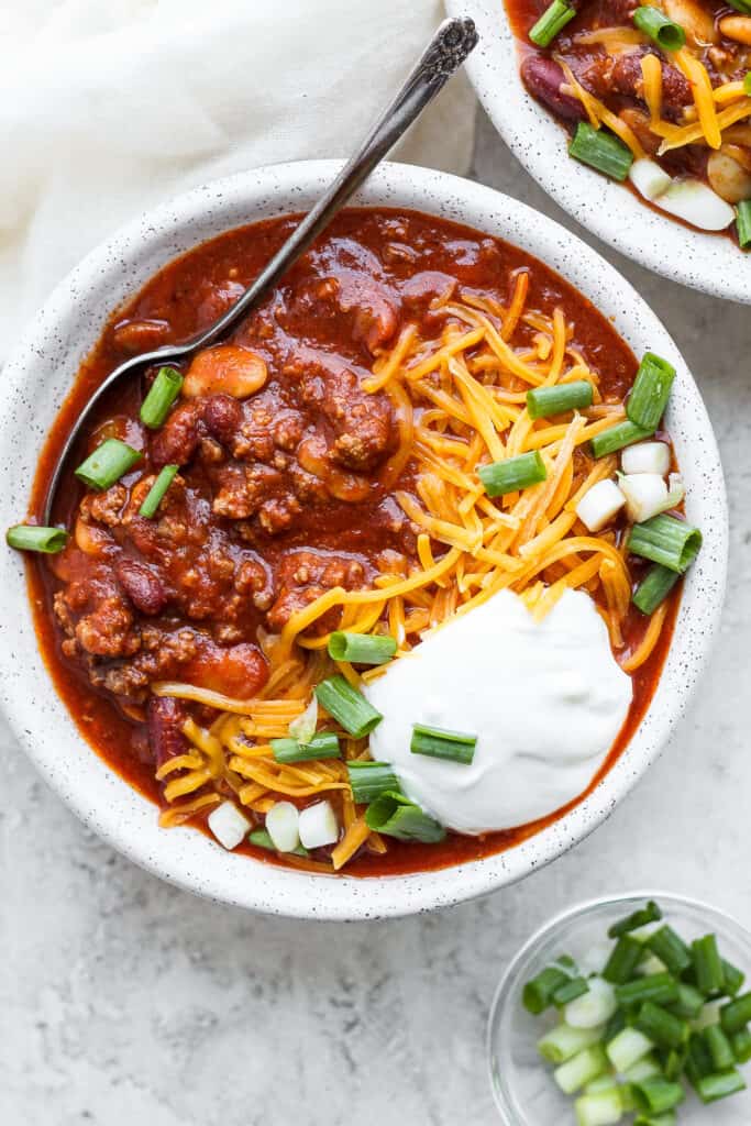 Slow cooker chili in a bowl topped with sour cream, shredded cheese and diced green onion.