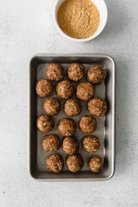 energy balls on a baking sheet next to a bowl of peanut butter.