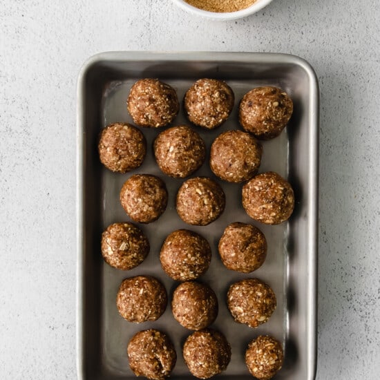 energy balls on a baking sheet next to a bowl of peanut butter.