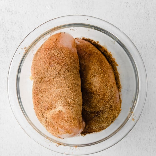two pieces of chicken in a glass bowl on a white surface.