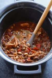 Crockpot chicken chili with a wooden spoon in it.