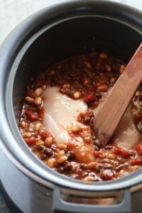 A crockpot full of chili and beans with a wooden spoon.