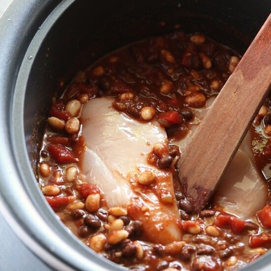 A crockpot full of chili and beans with a wooden spoon.