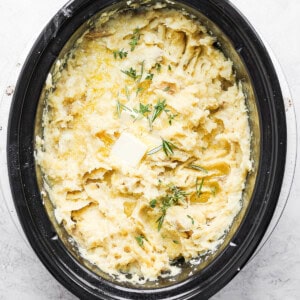 A crock pot filled with mashed potatoes and dill.