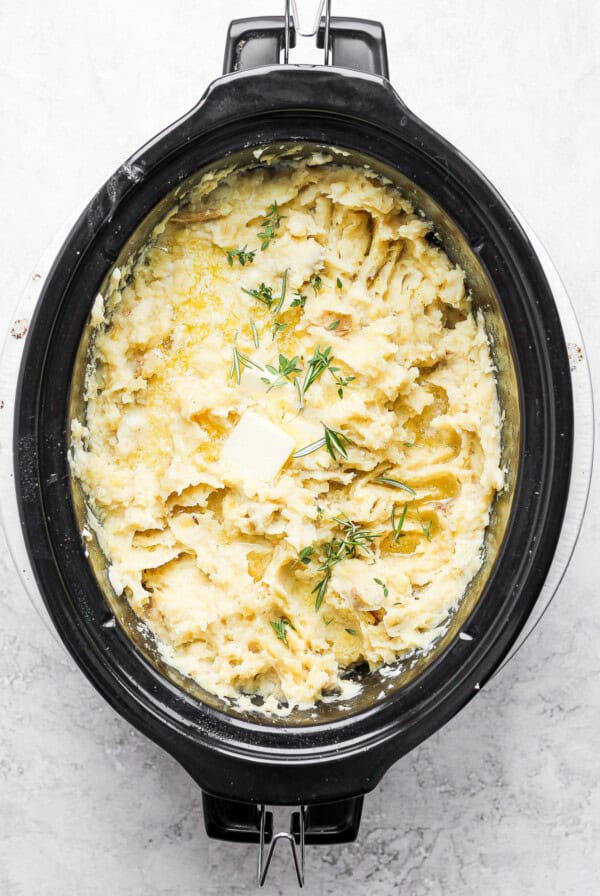 A crock pot filled with mashed potatoes and dill.