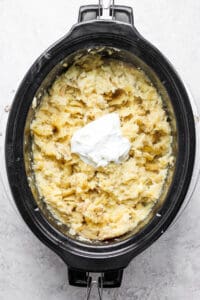 A crock pot filled with mashed potatoes and sour cream.