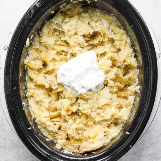 A crock pot filled with mashed potatoes and sour cream.