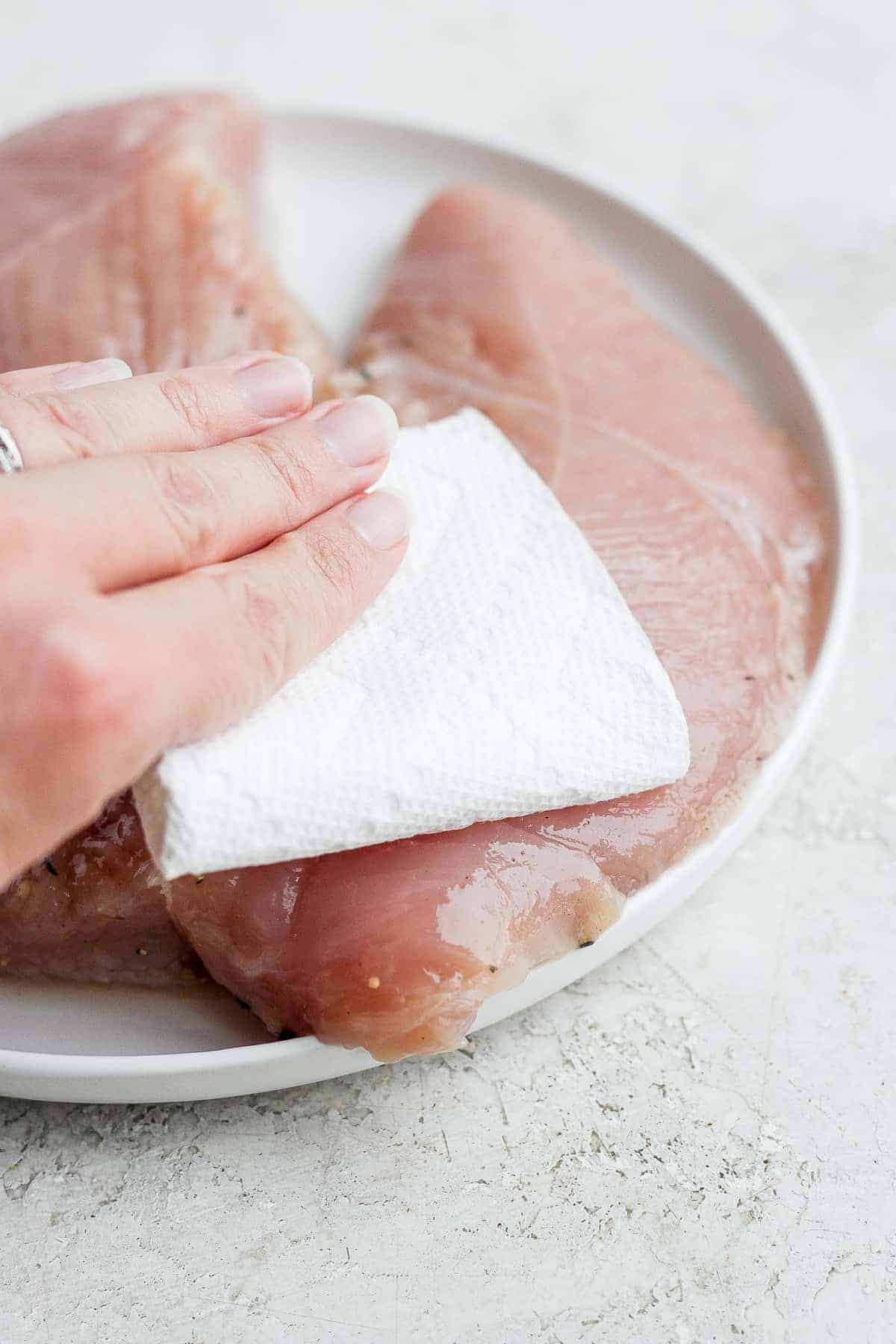 hand patting turkey tenderloin on plate.