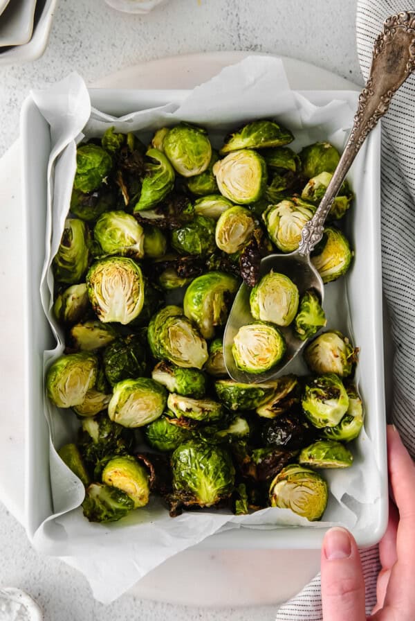 Roasted brussels sprouts in a white dish with a spoon.