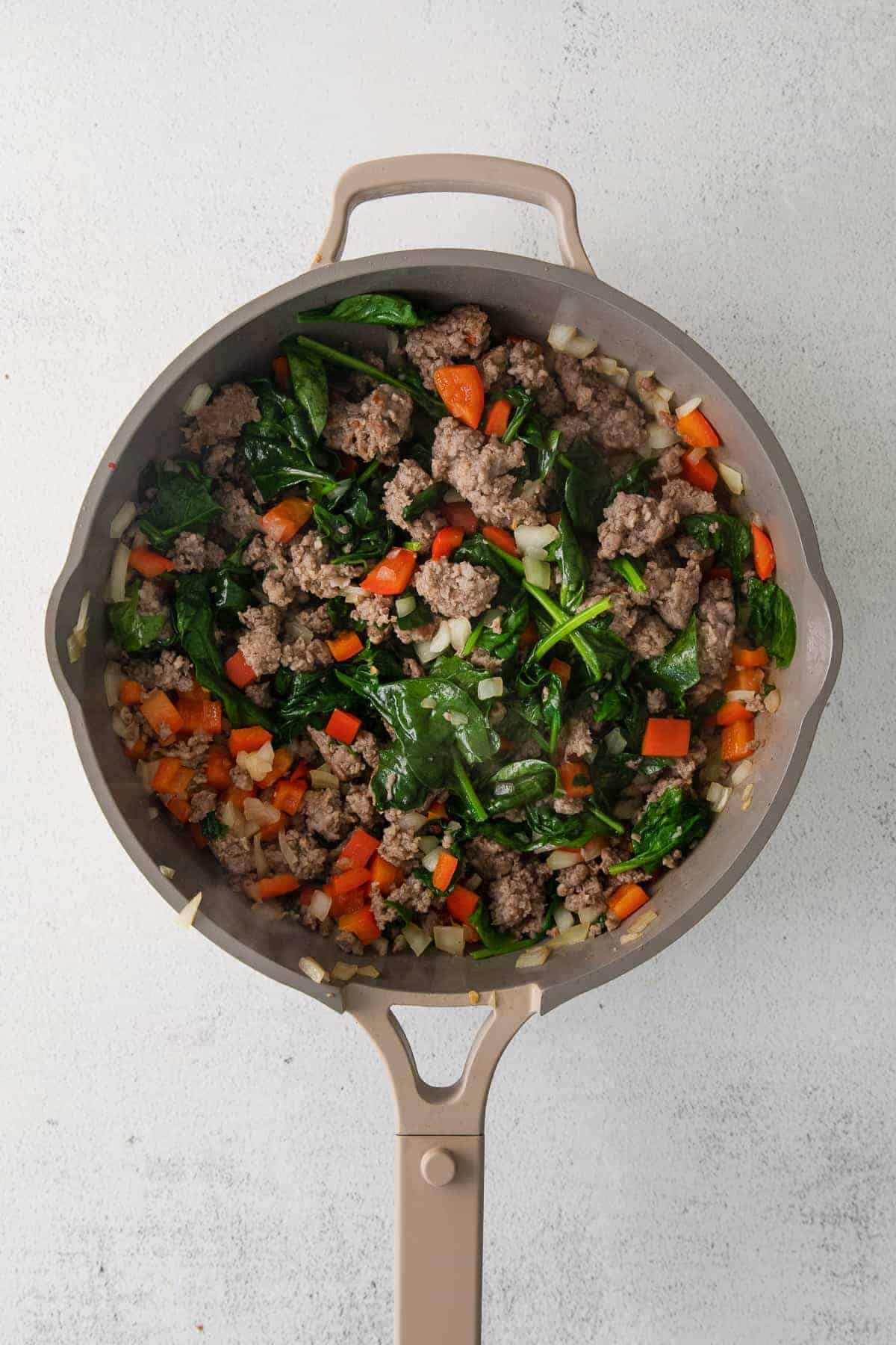 Sausage, onion, peppers, and spinach in a skillet. 