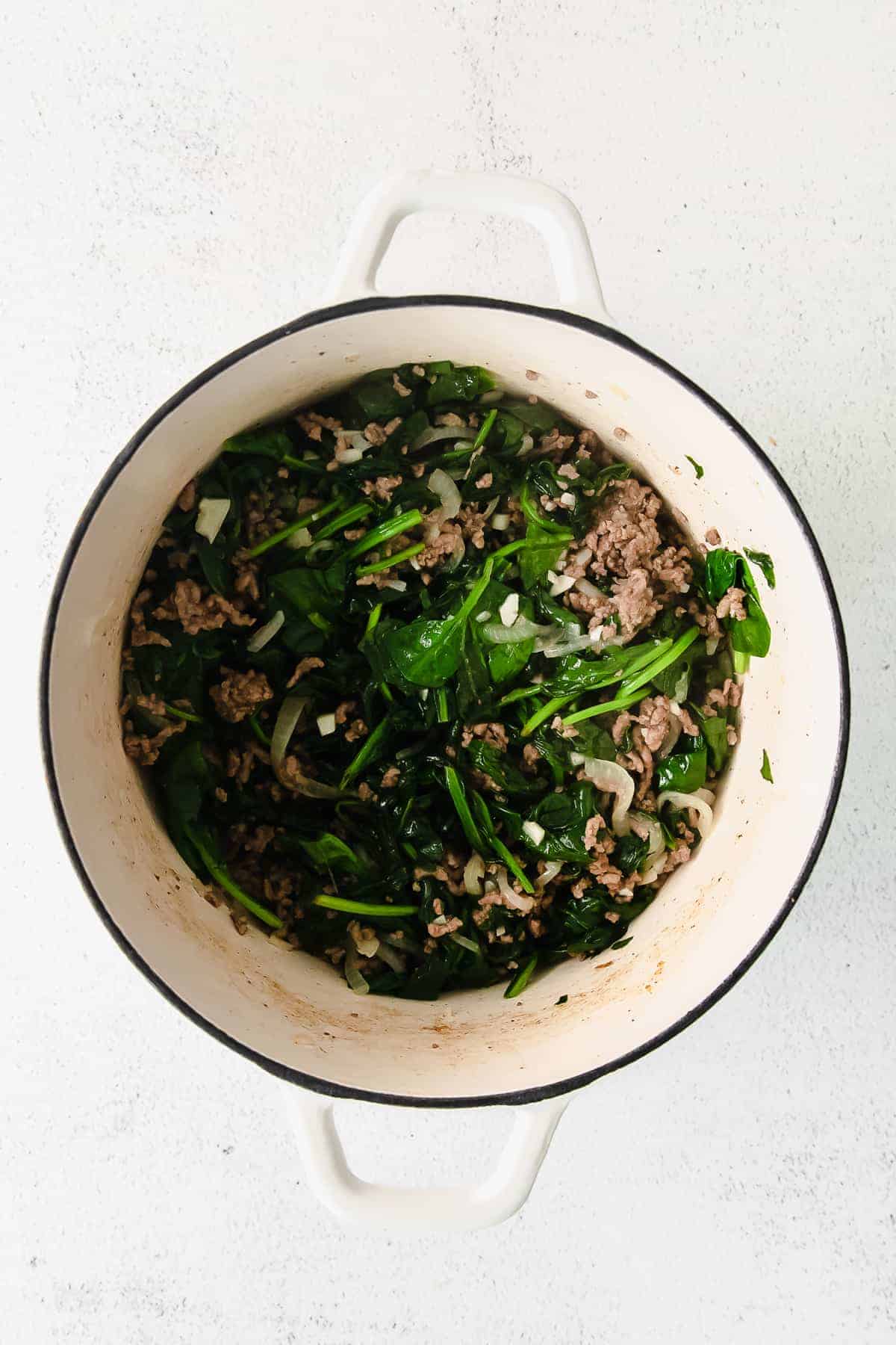 Meat, spinach, and onion in a dutch oven. 