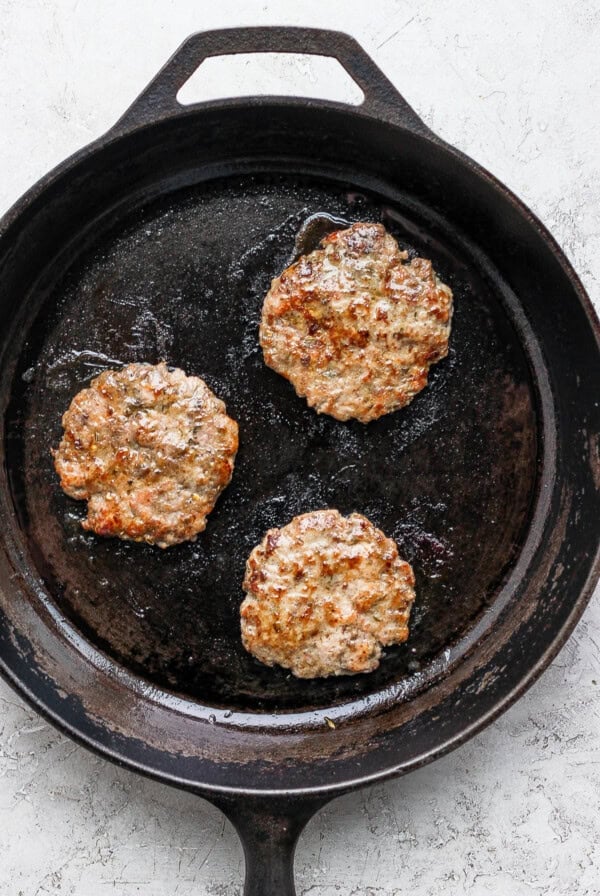 Three patties in a cast iron skillet on a white surface.