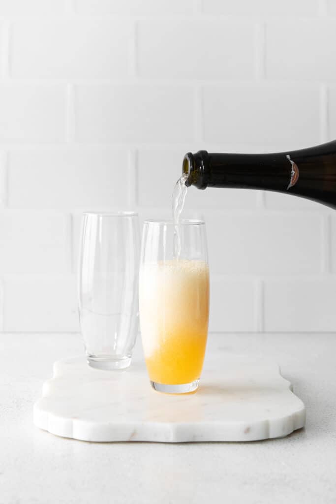 champagne being poured into a glass over orange juice
