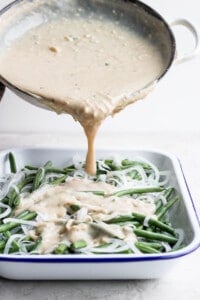 A sauce being poured over green beans in a white dish.