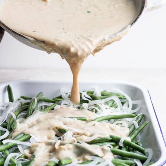 A sauce being poured over green beans in a white dish.