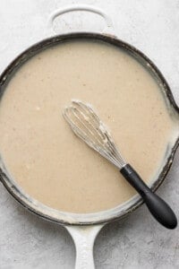 A skillet full of gravy with a whisk in it.