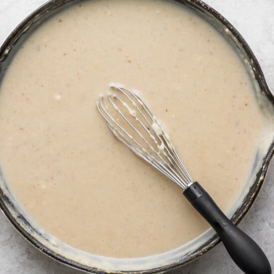 A skillet full of gravy with a whisk in it.
