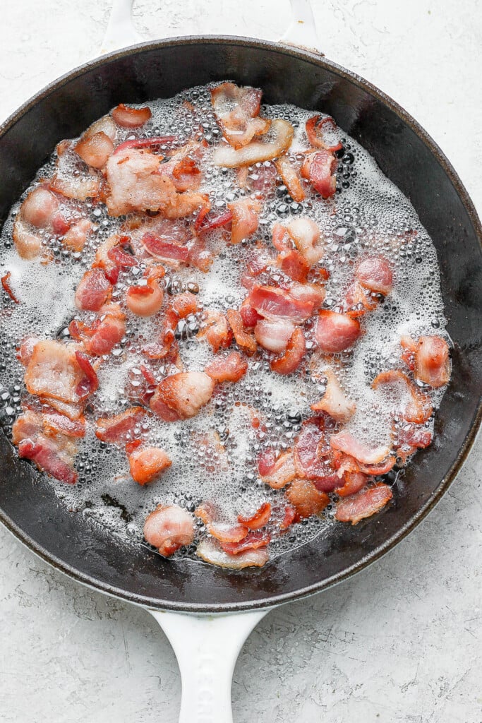 bacon slices being cooked in a cast iron skillet