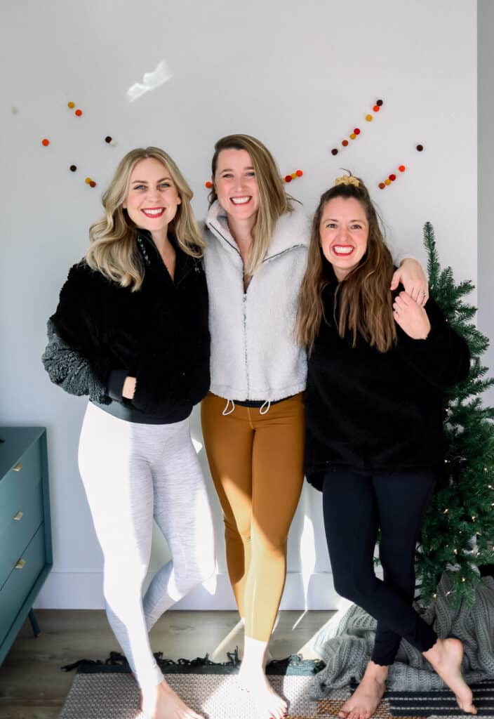 three women smiling in front of a christmas tree wearing lululemon