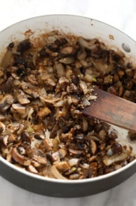 Sauteed mushrooms in a pan with a wooden spoon.