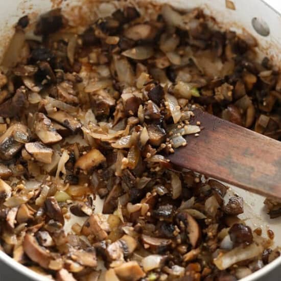 Sauteed mushrooms in a pan with a wooden spoon.