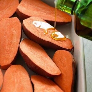 Sweet potatoes bring drizzled with olive oil in a baking dish.