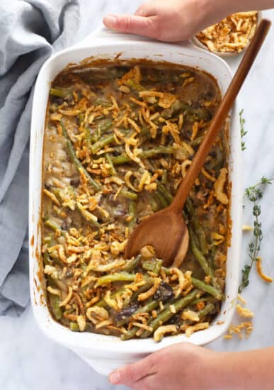 Green bean casserole in a white dish with a wooden spoon.
