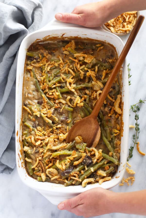 Green bean casserole in a white dish with a wooden spoon.