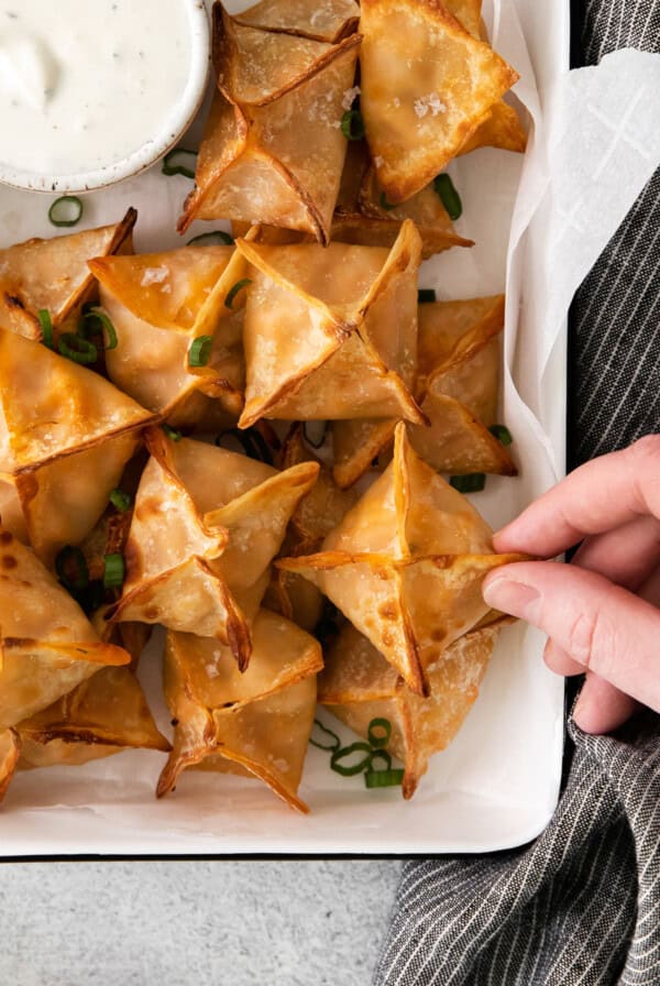 A person is holding a plate of fried wontons with dipping sauce.