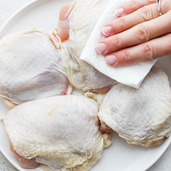 A person is wiping the skin off of chicken breasts on a plate.