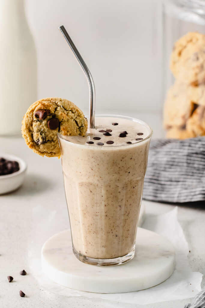 Cookie dough smoothie in a glass with a chocolate chip cookie on the rim. 