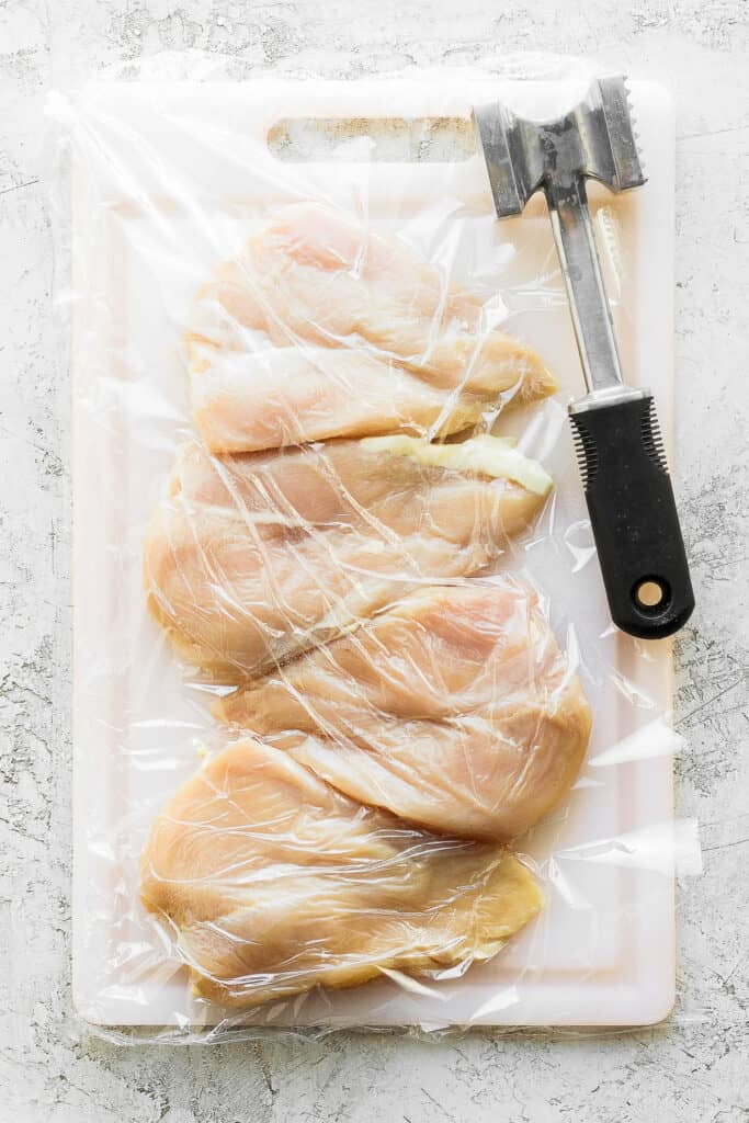 raw chicken breasts on a cutting board with a meat tenderizer