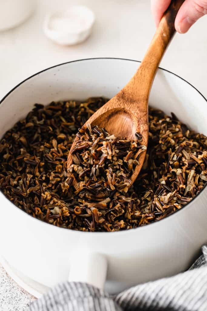 wooden spoon stirring a pot of cooked wild rice