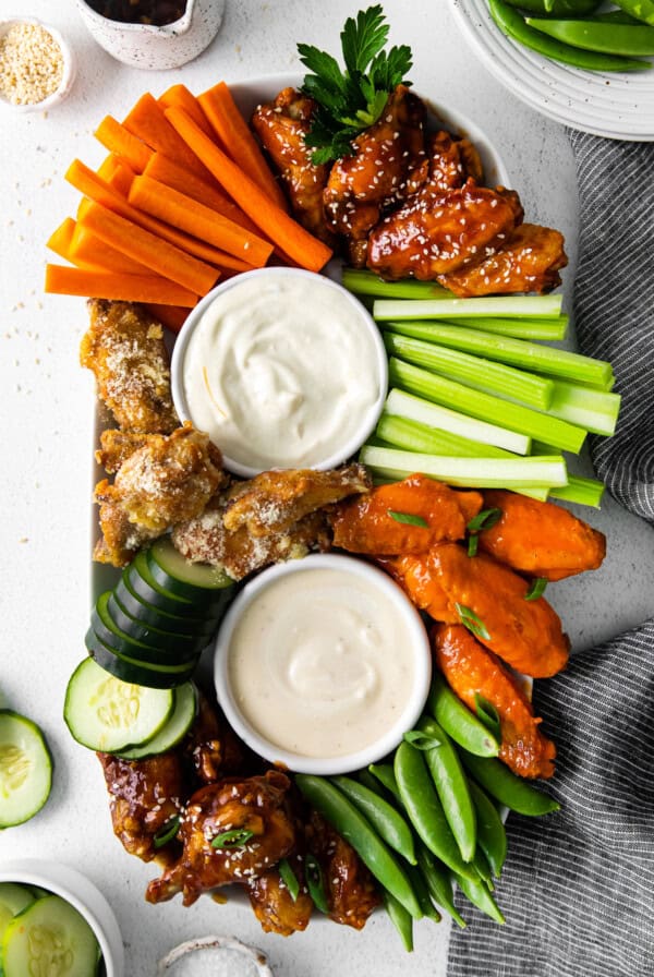 A tray with chicken wings, carrots, cucumbers and dip.
