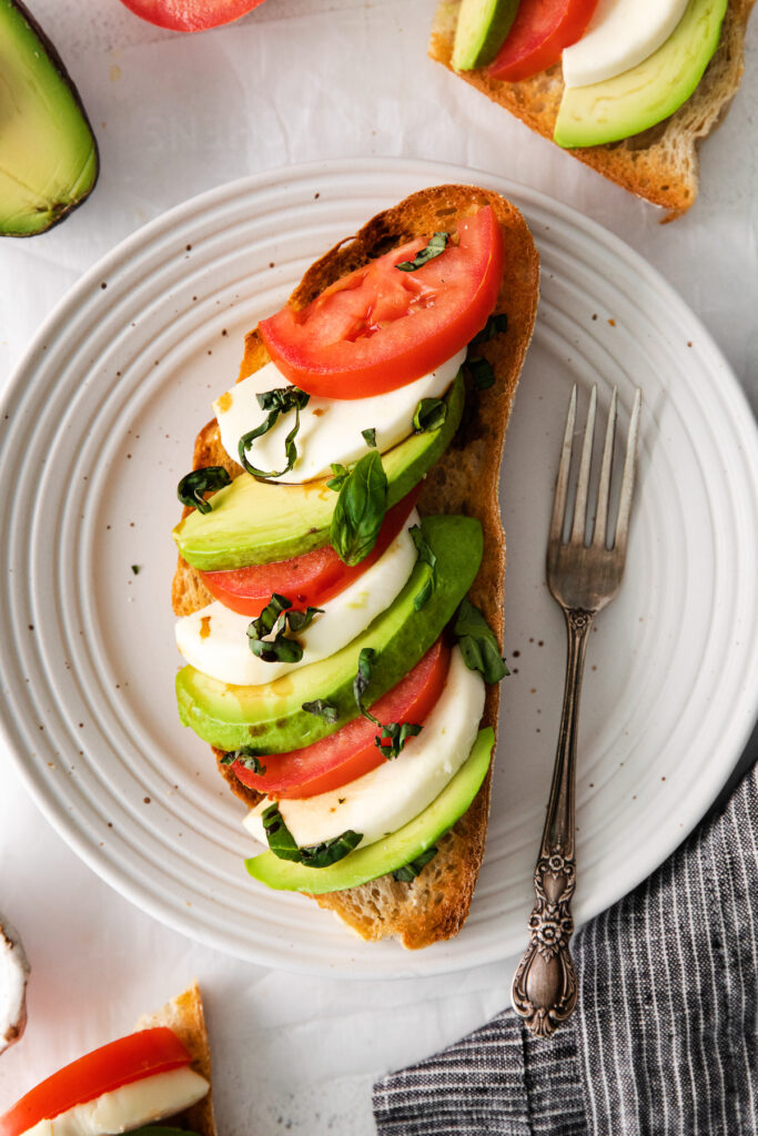 caprese ingredients on top of avocado toast on a plate