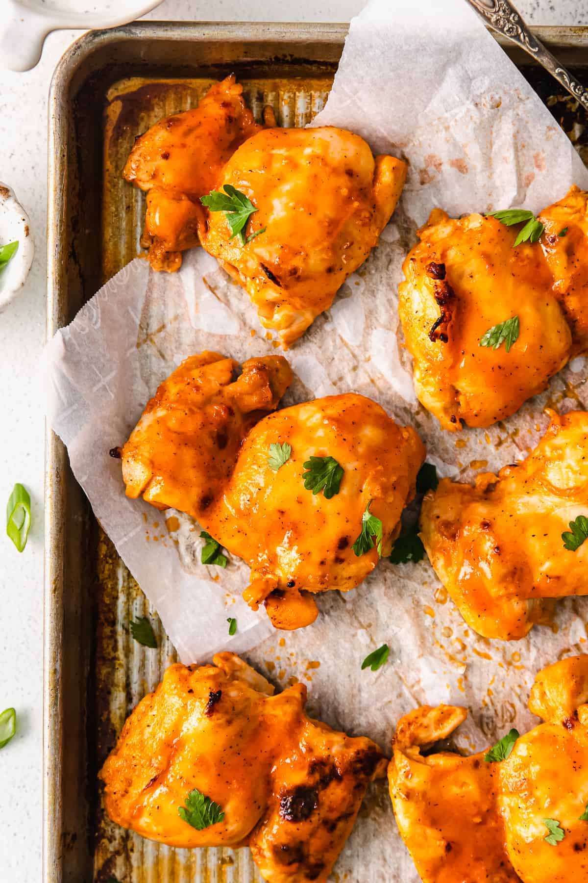 buffalo baked chicken thighs on a baking sheet topped garnished with parsley