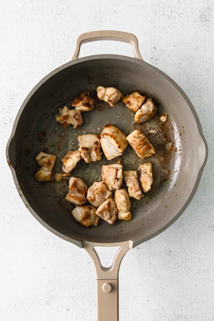 Chicken thighs browning in a skillet pan.