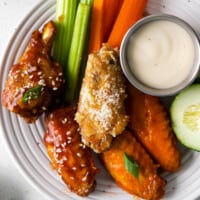 A plate with chicken wings, carrots, celery and dipping sauce.