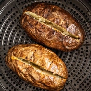Two baked potatoes in an air fryer.