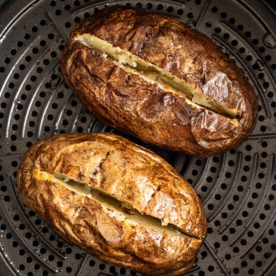 Two baked potatoes in an air fryer.