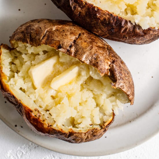 Two baked potatoes with butter on a plate.