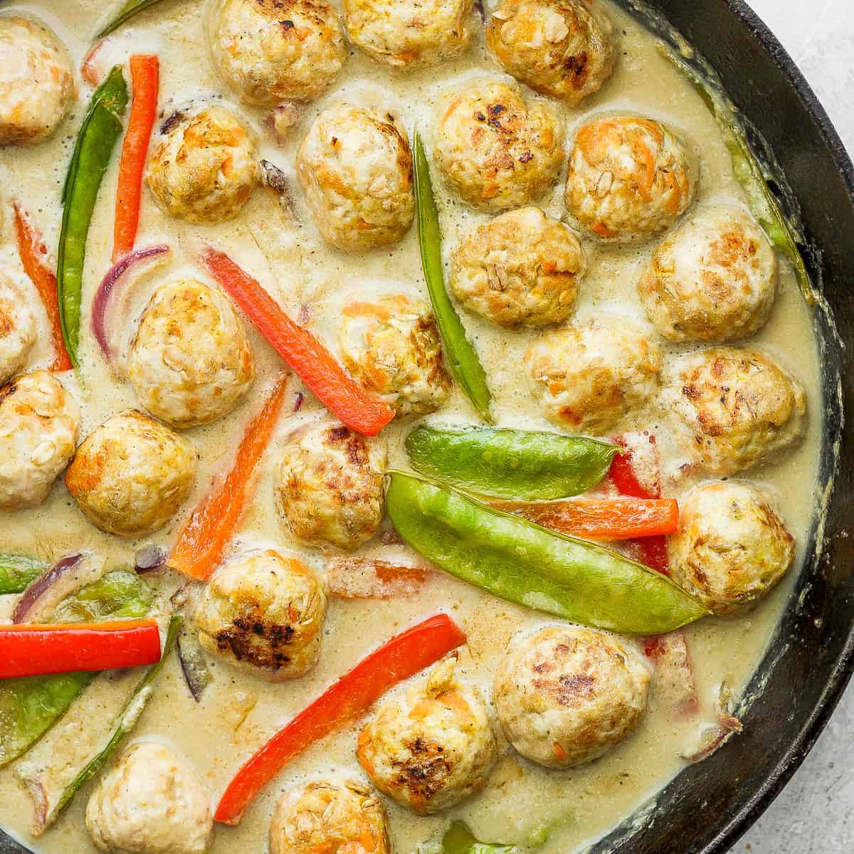 Chicken meatballs and vegetables simmering in a cast iron pan. 