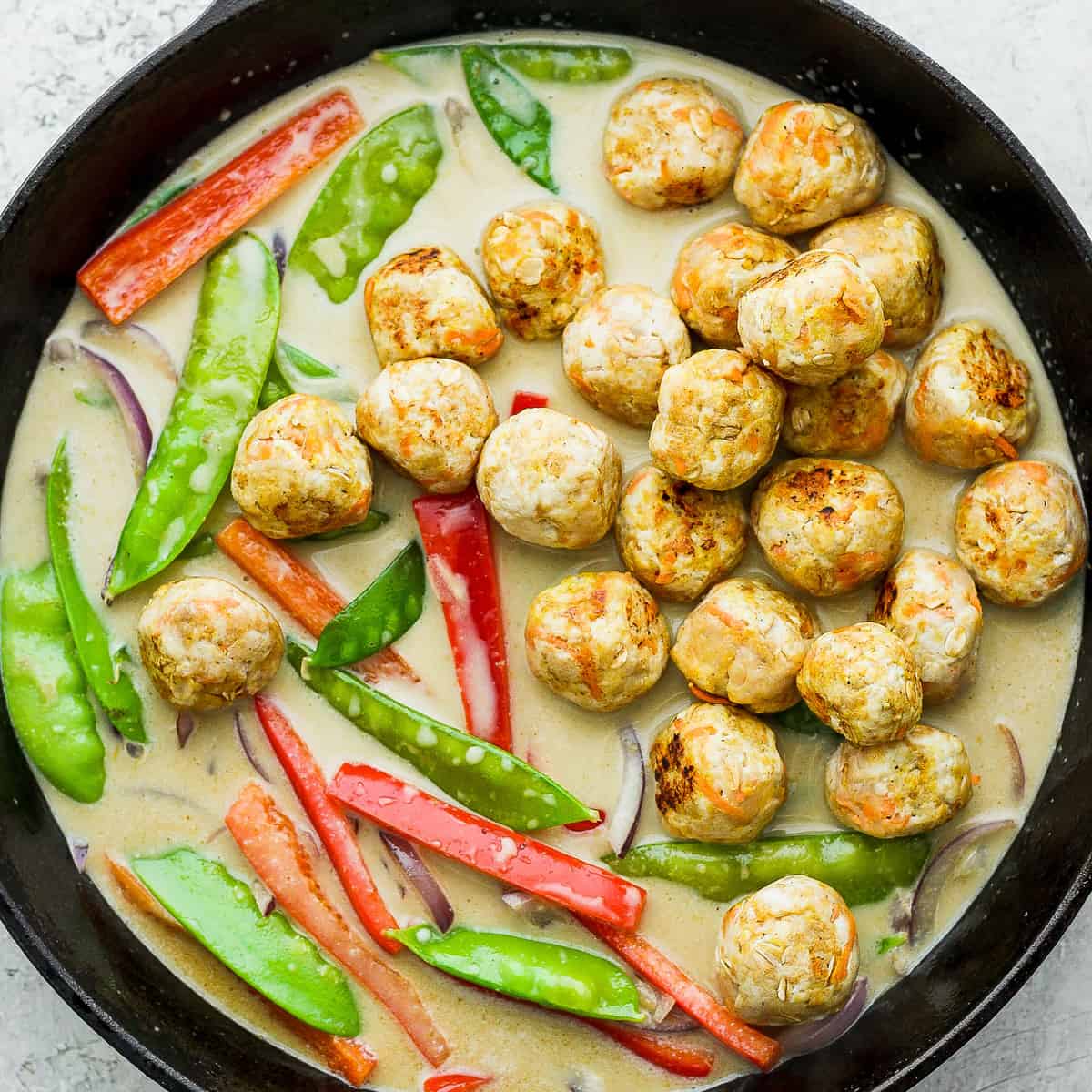 Green curry chicken meatballs and vegetables in a cast iron skillet. 