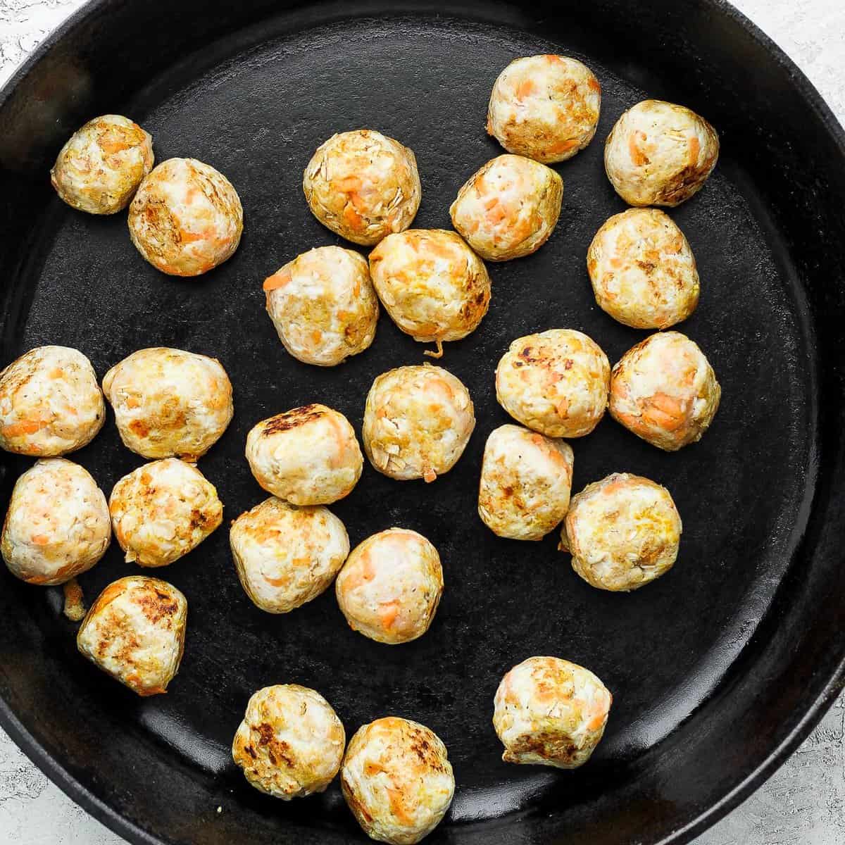 Chicken meatballs browning in a cast iron pan. 