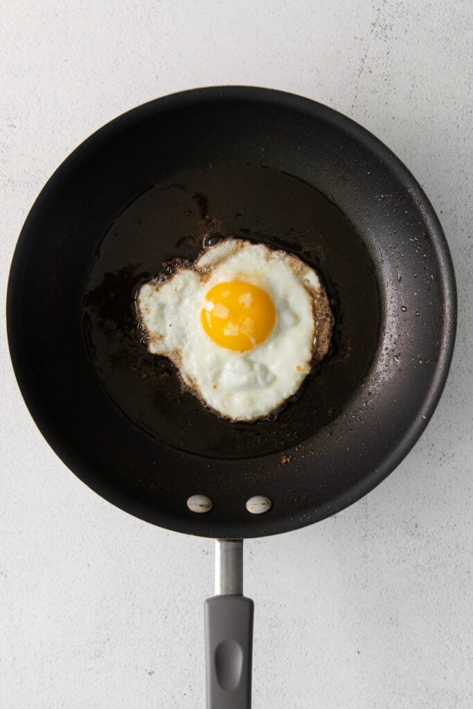 An egg frying in oil in a nonstick pan. 