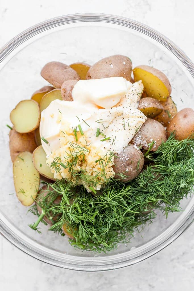 Potatoes, mayo, garlic, and fresh dill in a bowl. 