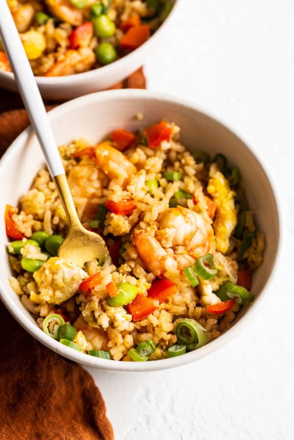 A bowl of shrimp fried rice with vegetables and a spoon.