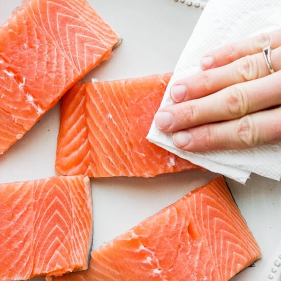 A person is holding a piece of salmon on a plate.